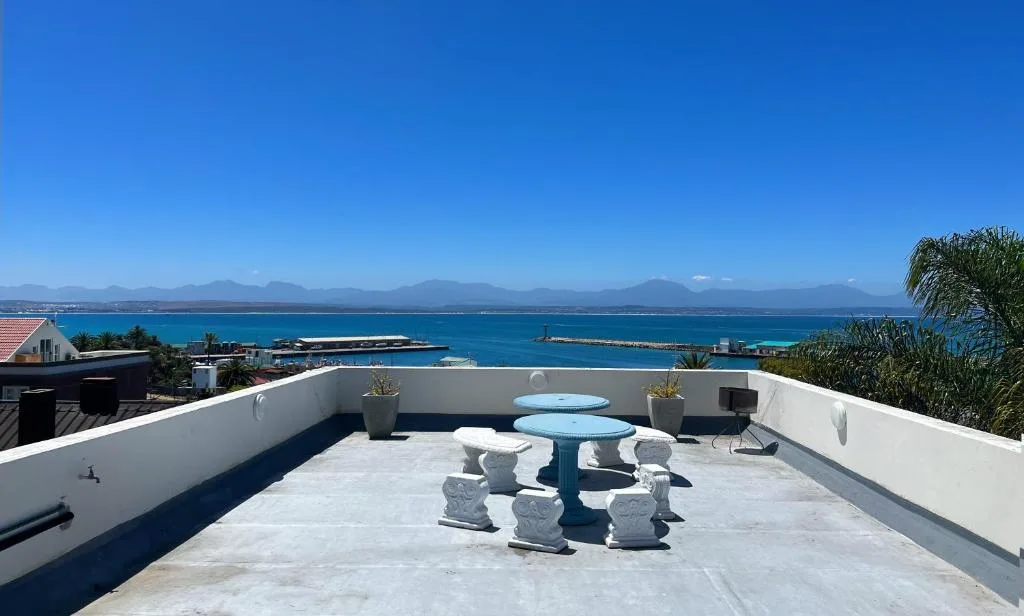 Panoramic ocean and mountain vista from elevated terrace with seating area