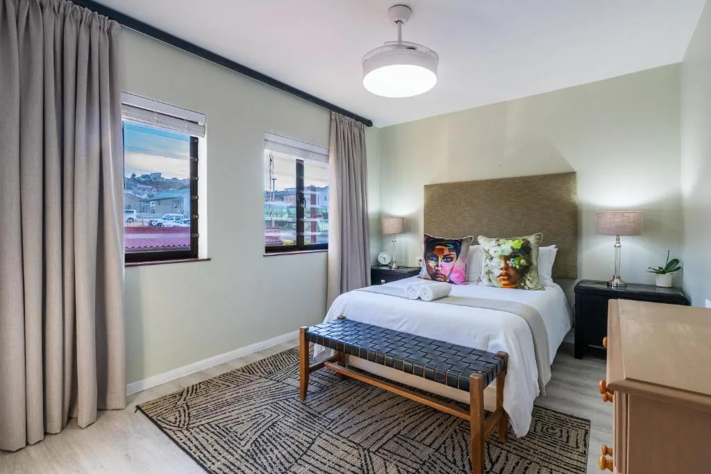 Bright bedroom with queen bed, modern furnishings, and town views through windows