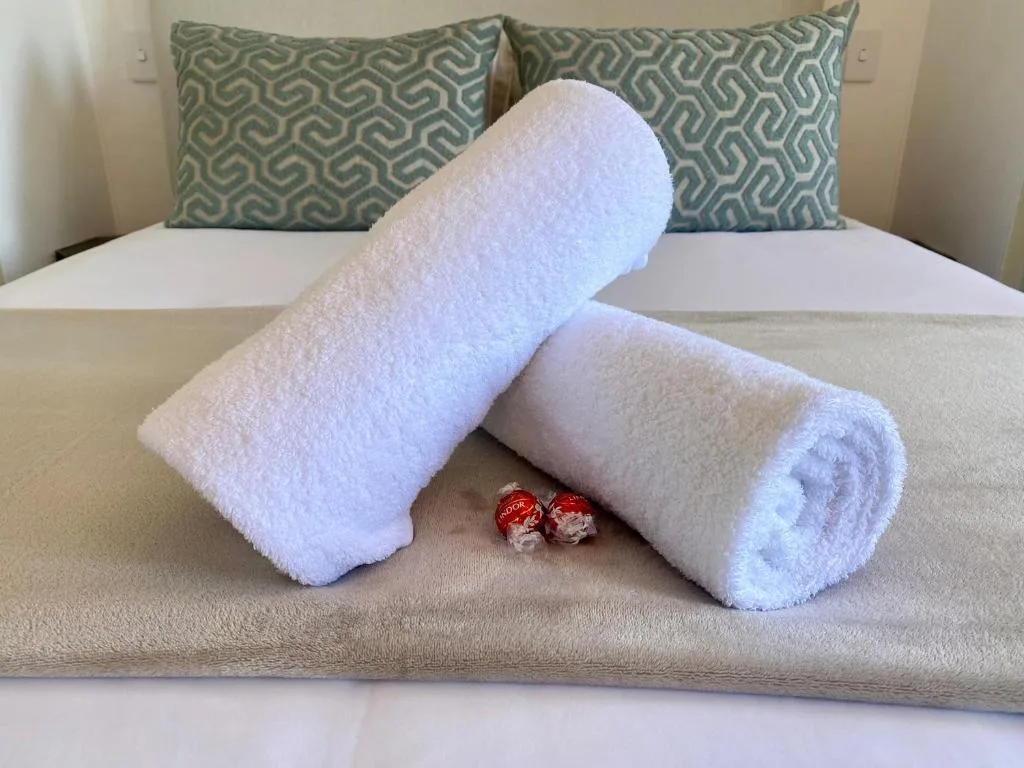 Rolled white towels with welcome chocolates on bedroom bed