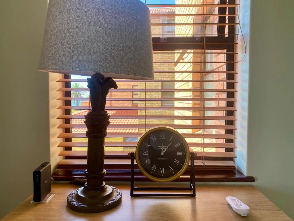 Decorative lamp and clock on windowsill with wooden blinds