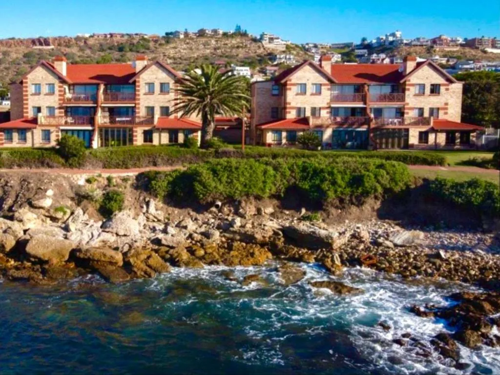 Beachfront apartment complex with red roofs overlooking rocky coastline and waves