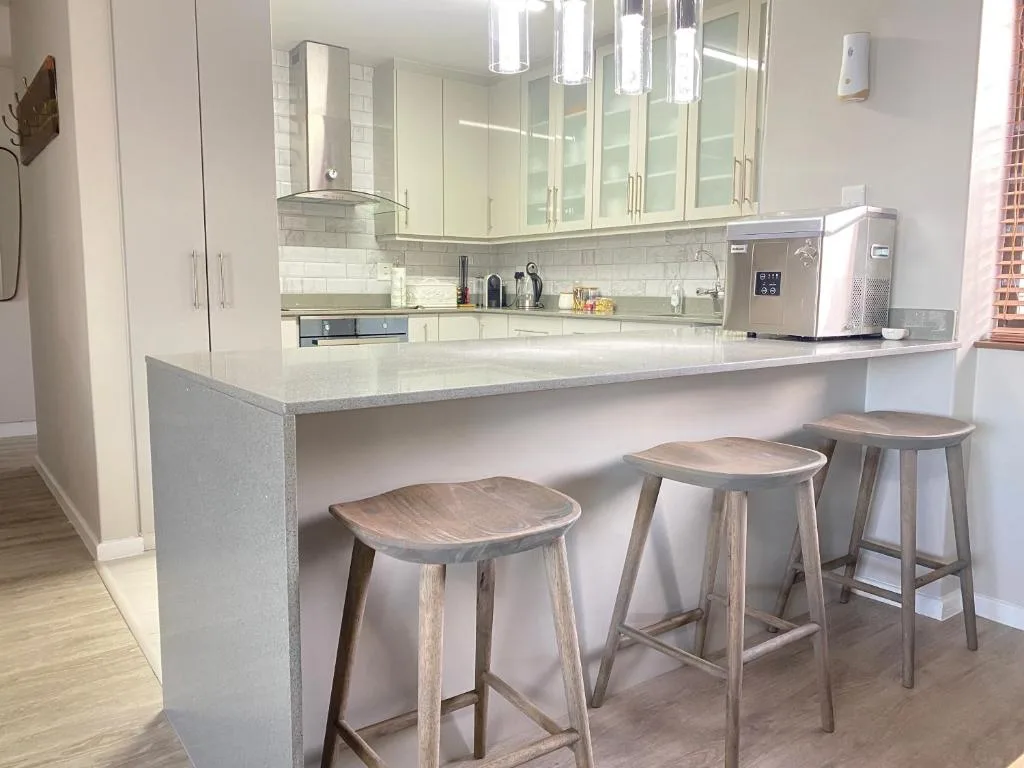 Modern kitchen with white cabinetry, grey countertop, and wooden bar stools