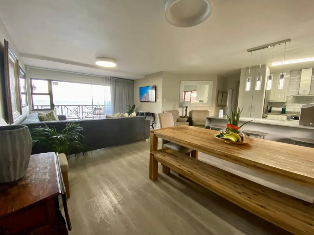 Open-plan lounge and dining area with sofa, wooden table, and ocean views