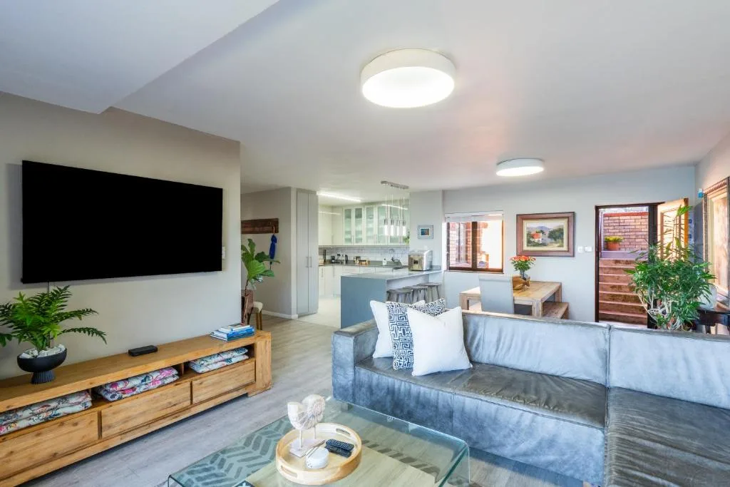 Modern open-plan lounge with gray sofa, wall-mounted TV, and kitchen visible beyond