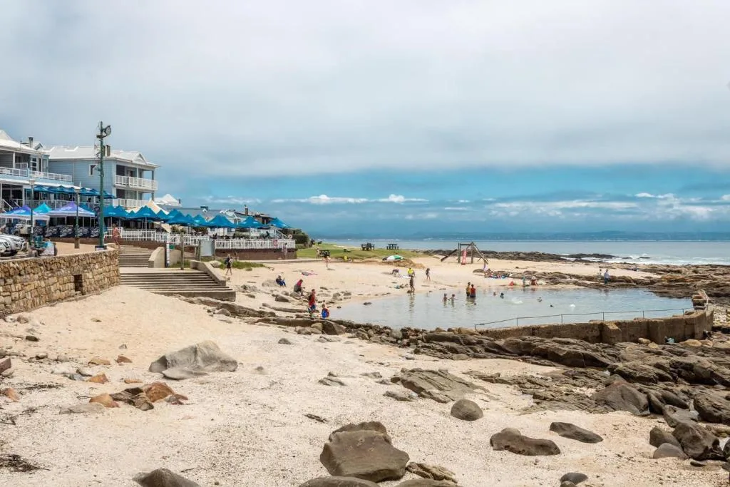 Coastal beachfront with tidal pool, sandy shore, and distant mountains