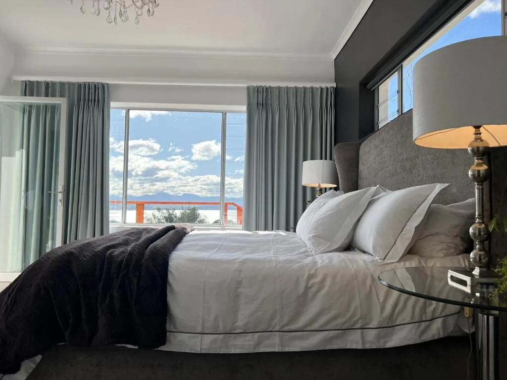 Modern bedroom with white bedding overlooking coastal lagoon view through large windows