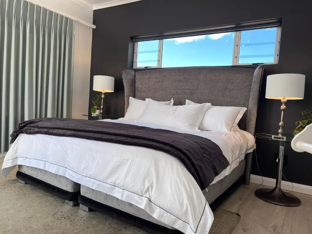 Modern bedroom with grey upholstered bed, white linens, and skyline views