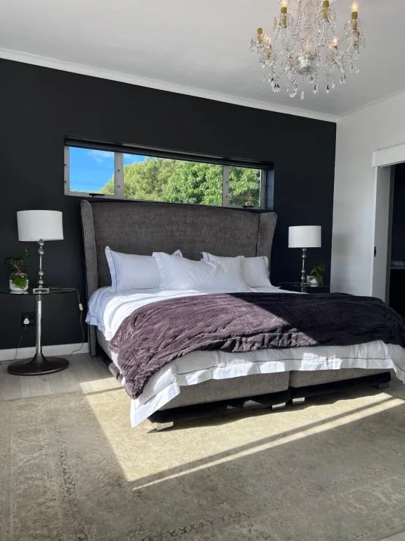 Modern bedroom with dark accent wall, king bed, crystal chandelier, and nature views