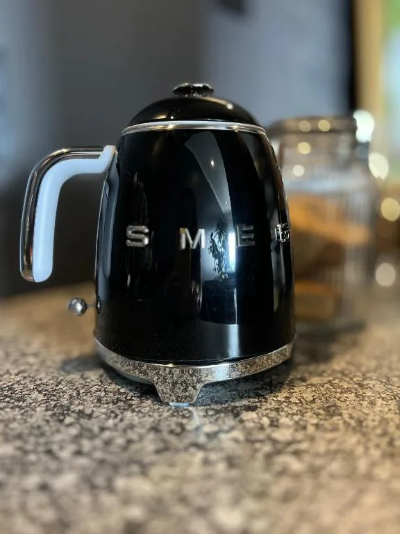 Black SMEG electric kettle on kitchen counter with blurred glasses
