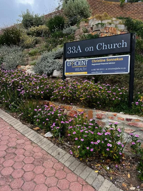 Property entrance sign with flowering gardens and brick building visible