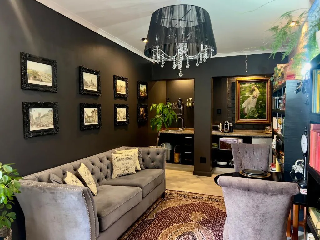 Elegant dark-walled lounge with plush gray sofa, chandelier, framed artwork, and contemporary furnishings