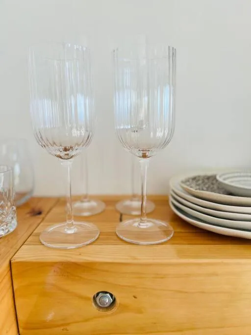 Two elegant ribbed wine glasses on wooden table with place settings nearby
