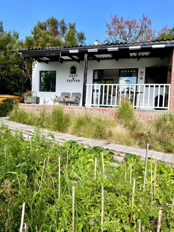 White cottage with black trim, white deck railing, and vegetable garden