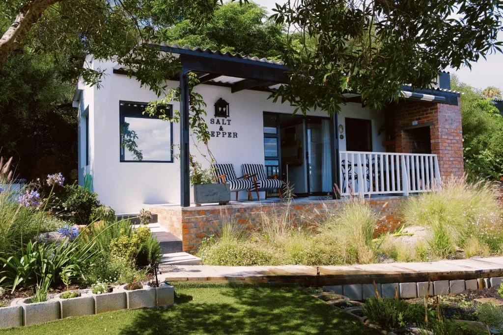 Modern white cottage with blue trim and brick base, surrounded by native garden plantings