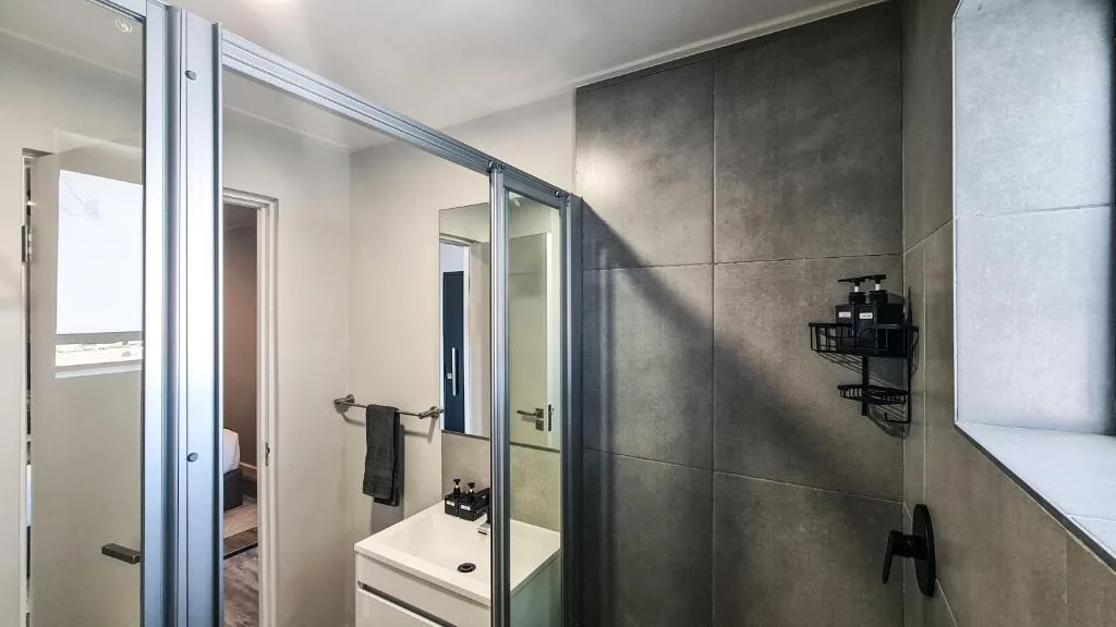 Modern bathroom with grey tile walls, vanity sink, and glass shower enclosure