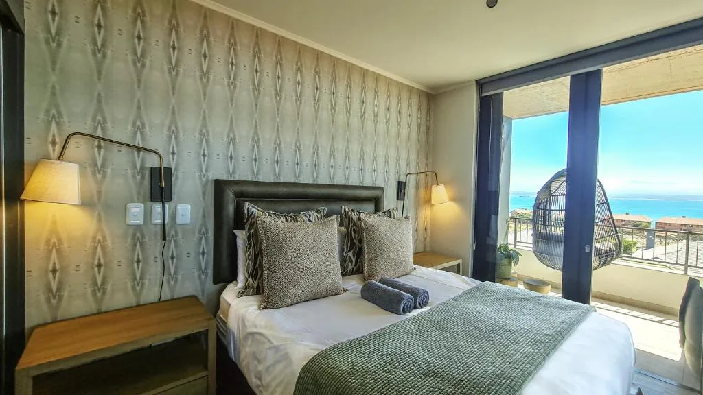Modern bedroom with ocean view through sliding glass doors and hanging chair