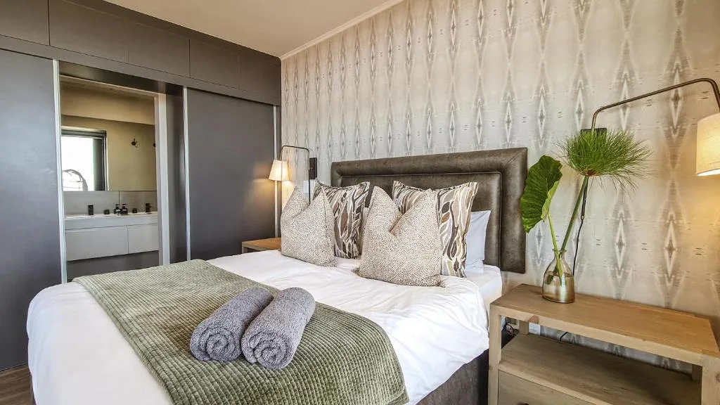 Modern bedroom with leather headboard, patterned wallpaper, ensuite bathroom visible
