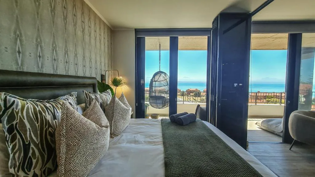 Modern bedroom with ocean view through floor-to-ceiling windows and hanging chair
