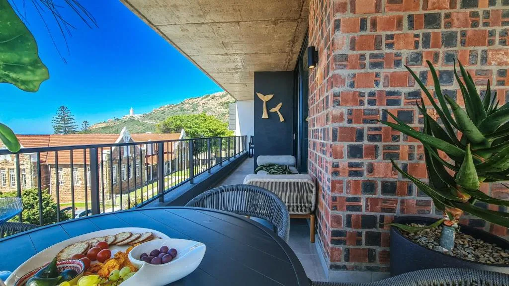 Seaside balcony with seating, food platter, and mountain views beyond