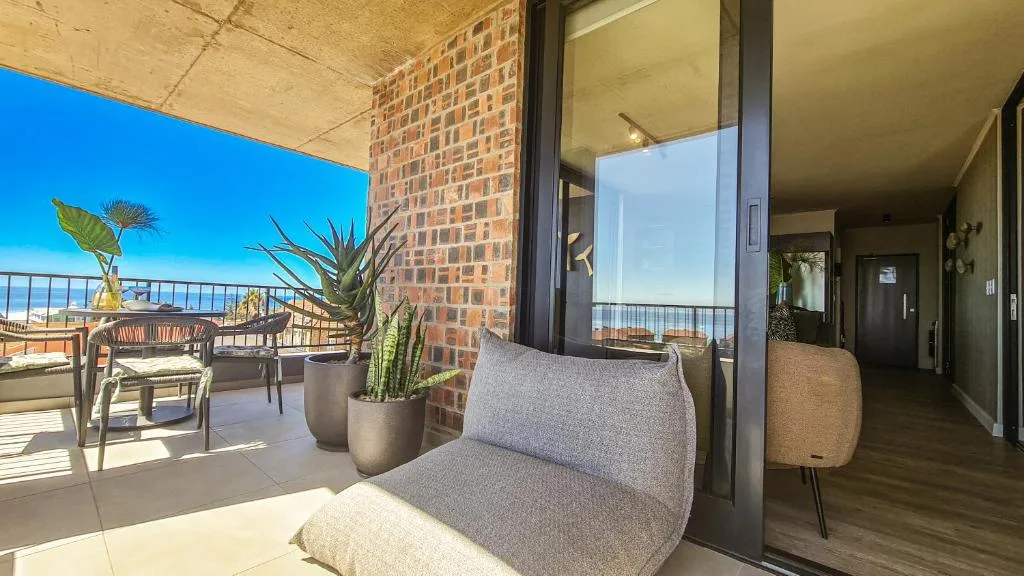 Modern penthouse balcony with seating, potted plants, and coastal views