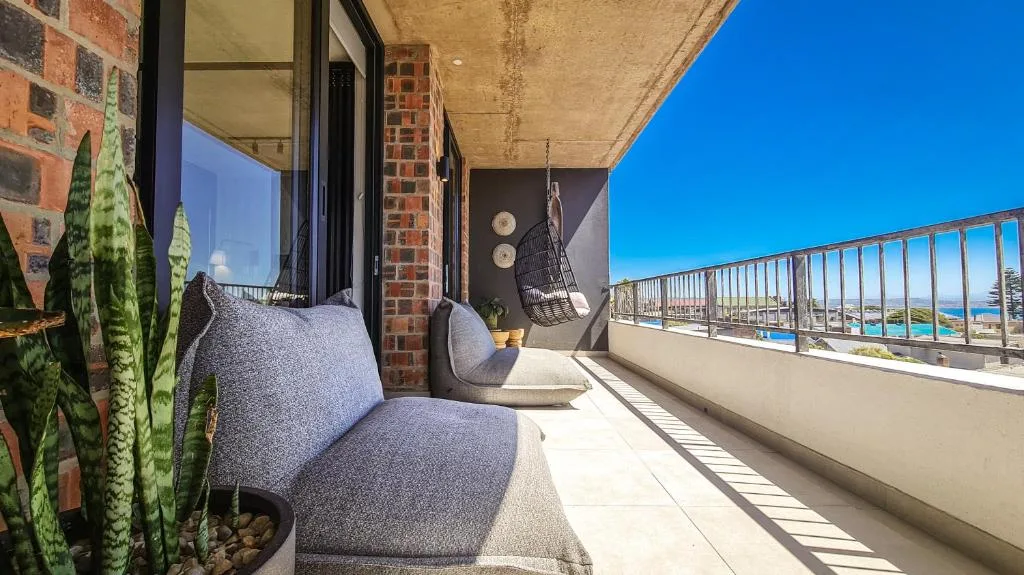 Modern balcony with gray seating, ocean and coastline views beyond railing