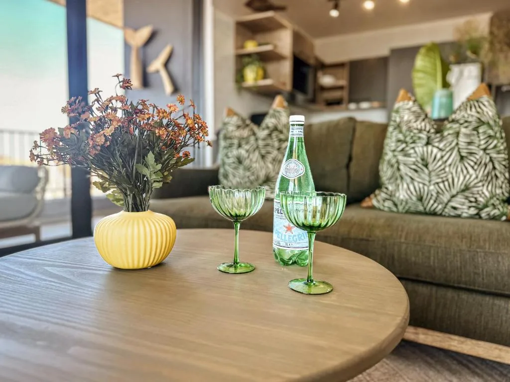 Yellow vase with dried flowers and green glassware on wooden table