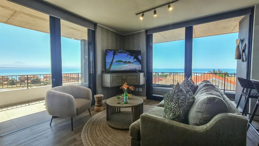 Modern lounge with ocean view, TV, comfortable seating, and panoramic windows