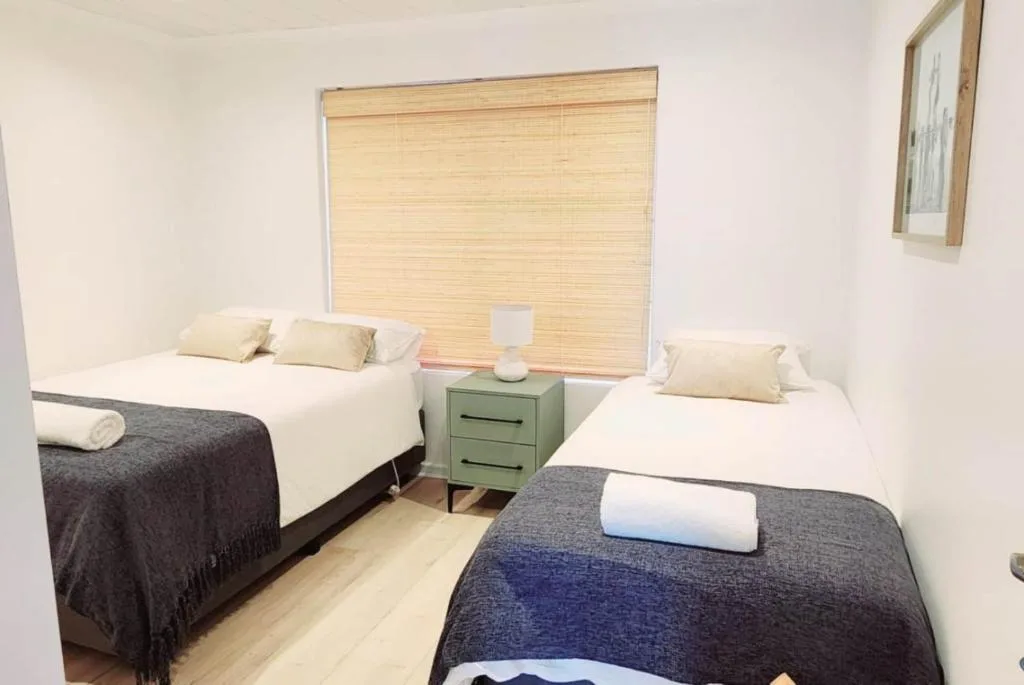 Twin bedroom with two single beds, green nightstand, and wooden blinds