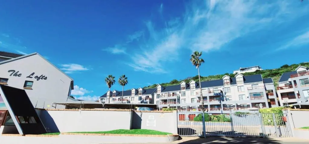 Modern white apartment buildings on hillside with palm trees and beach access