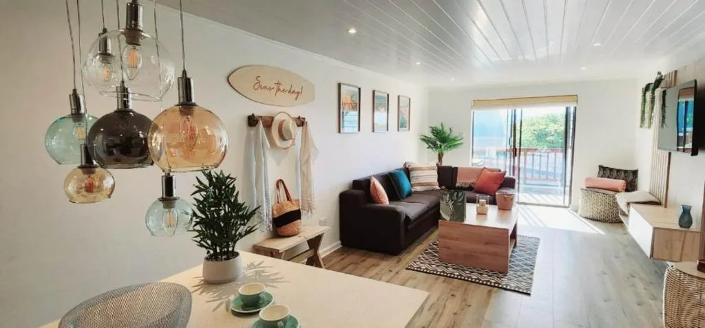 Bright open-plan living area with dark sofa, pendant lights, and ocean views