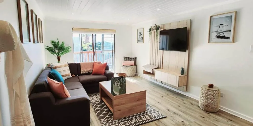 Spacious living room with dark sofa, TV, ocean view doors, and coastal decor