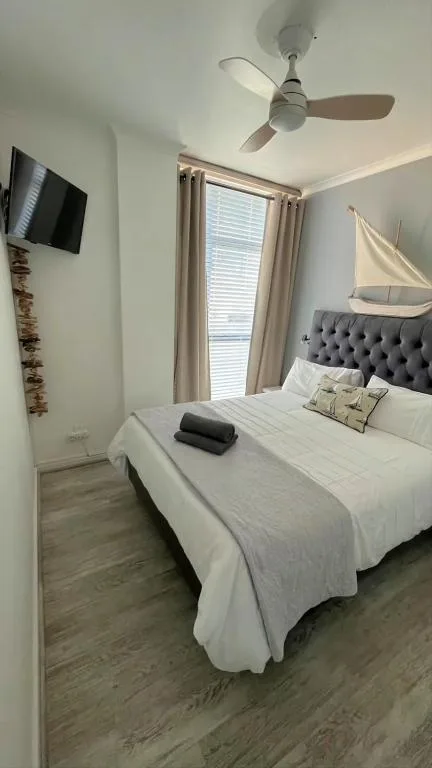 Bright bedroom with queen bed, gray upholstered headboard, ceiling fan