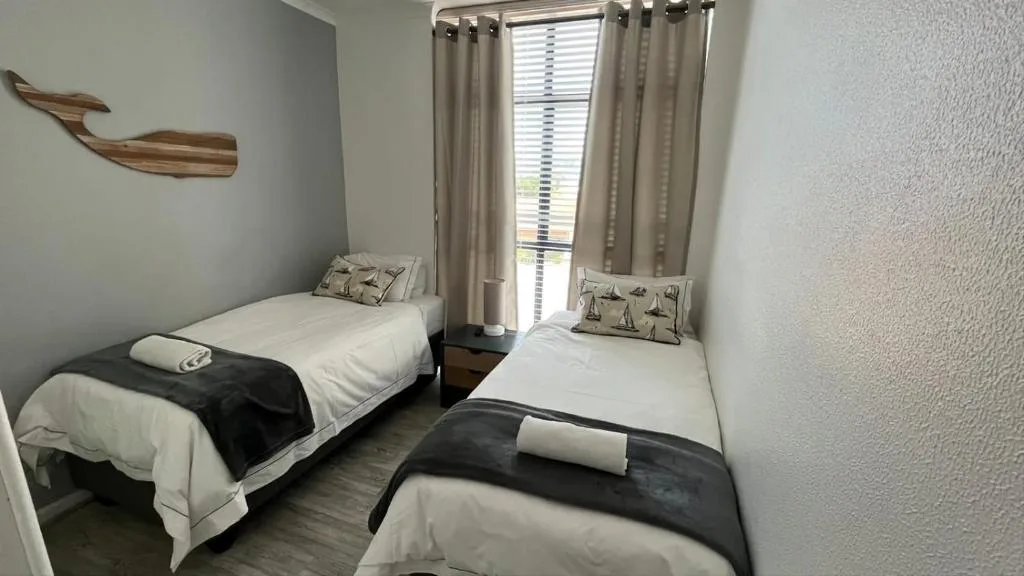 Twin bedroom with white bedding, neutral curtains, and wooden wall decor.