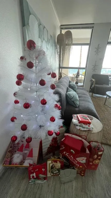 White Christmas tree with red ornaments beside gray sofa near window