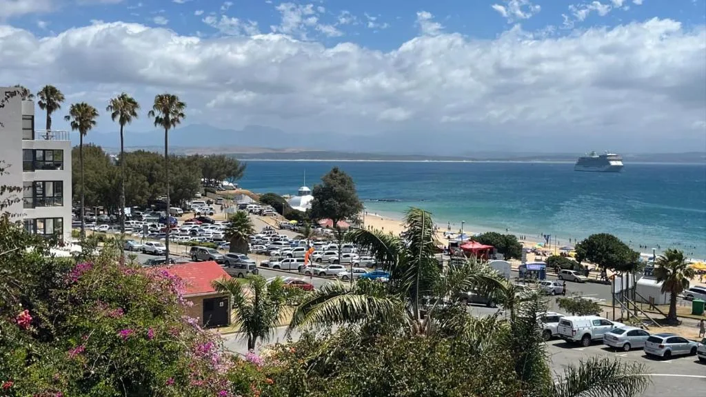 Coastal beach town view with turquoise ocean, palm trees, and cruise ship