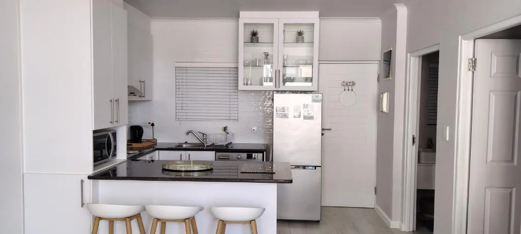 Modern white kitchen with black countertops, bar seating, and stainless appliances