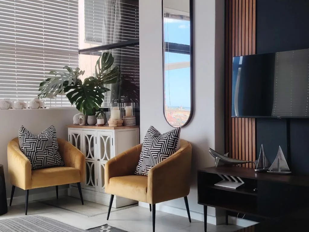 Modern lounge with golden armchairs, wall-mounted TV, and scenic coastal views