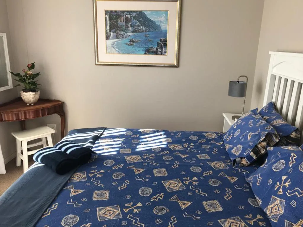 Bedroom with blue patterned bedding, wooden side table, and coastal artwork