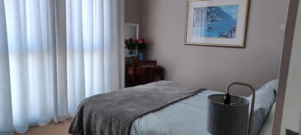 Spacious bedroom with queen bed, white curtains, wooden furniture, and coastal artwork