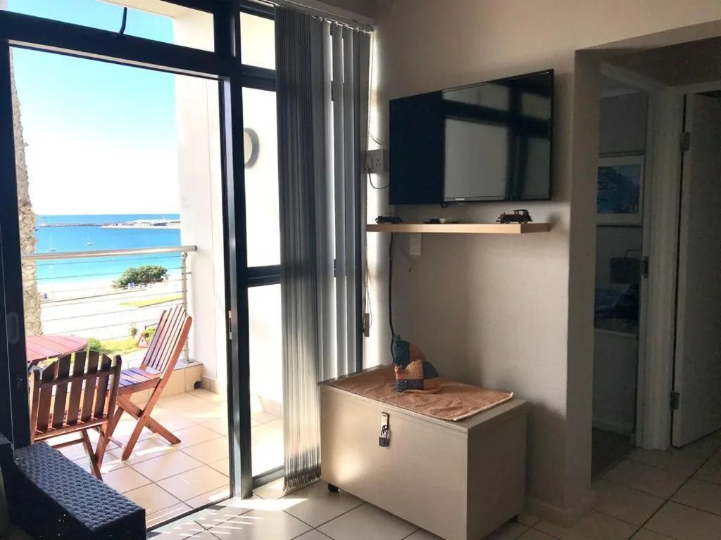 Modern lounge with wall-mounted TV, ocean view through sliding doors, wooden deck chairs