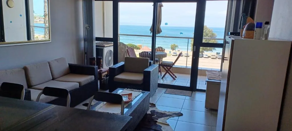 Bright lounge with gray sofa, ocean view through glass doors, coastal deck visible