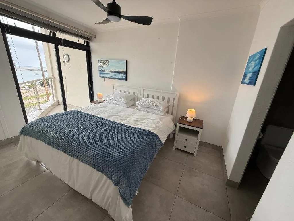 Bright bedroom with double bed, ocean view balcony, and ceiling fan