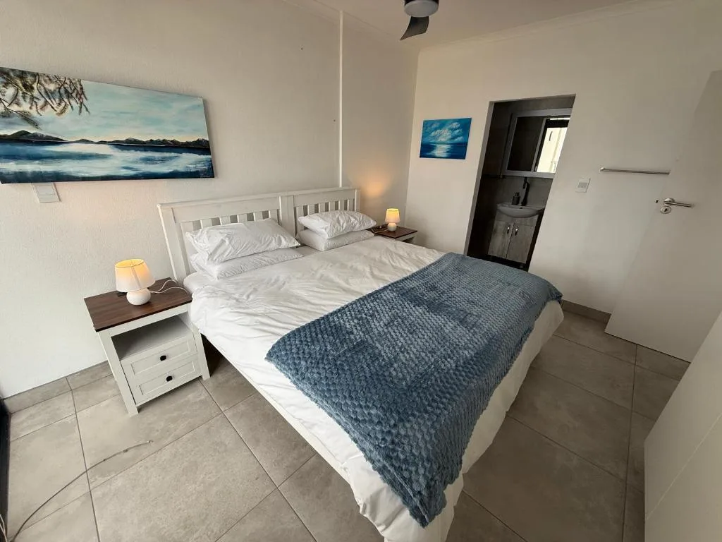 Spacious bedroom with queen bed, white headboard, blue throw, and ensuite bathroom