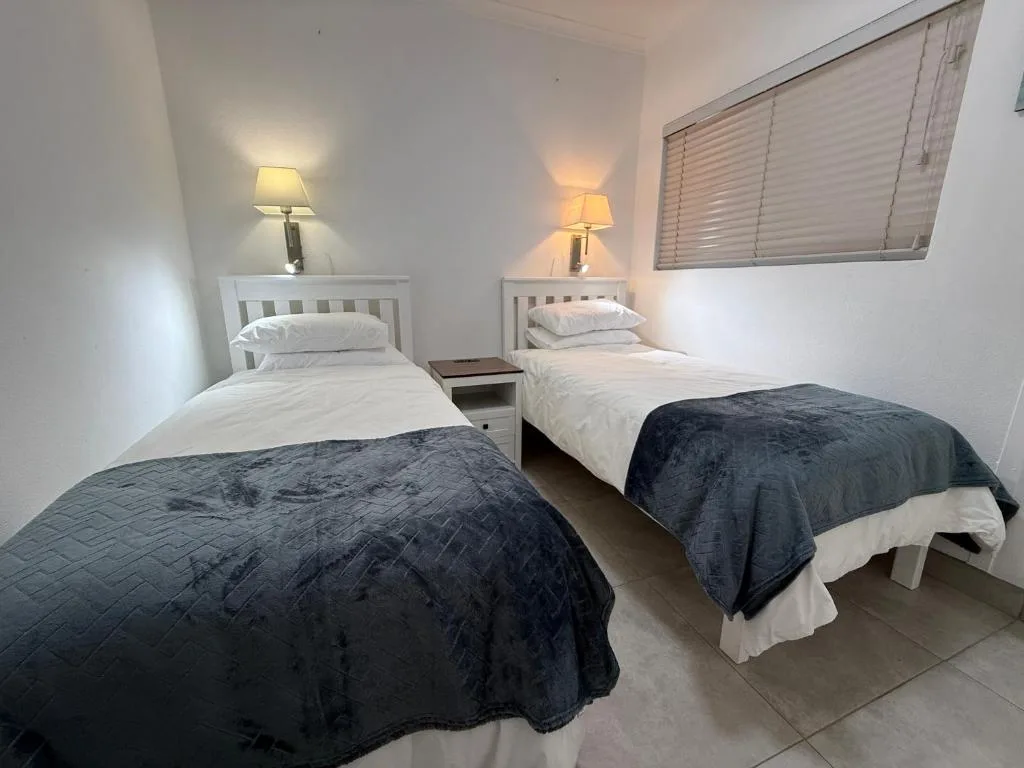 Twin bedroom with white wooden beds, dark quilts, and bedside lamps