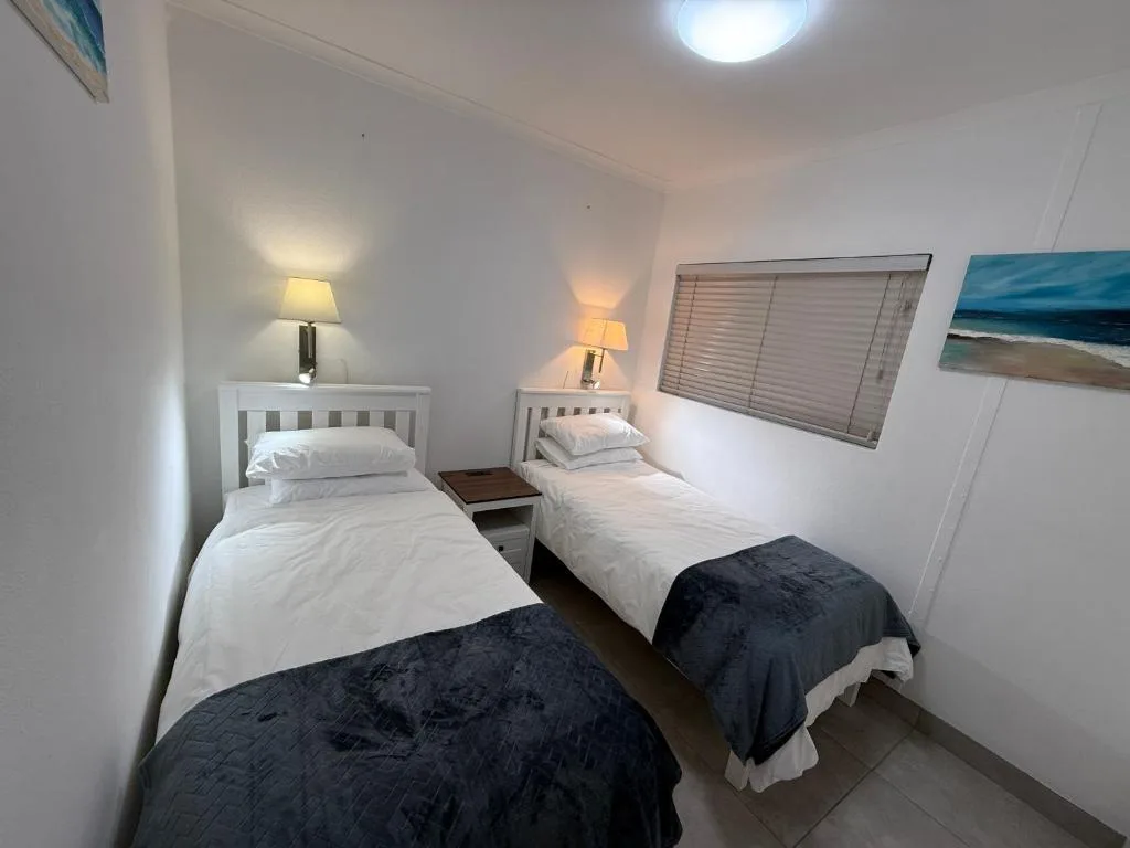 Twin bedroom with white headboards, bedside lamps, and ocean view artwork