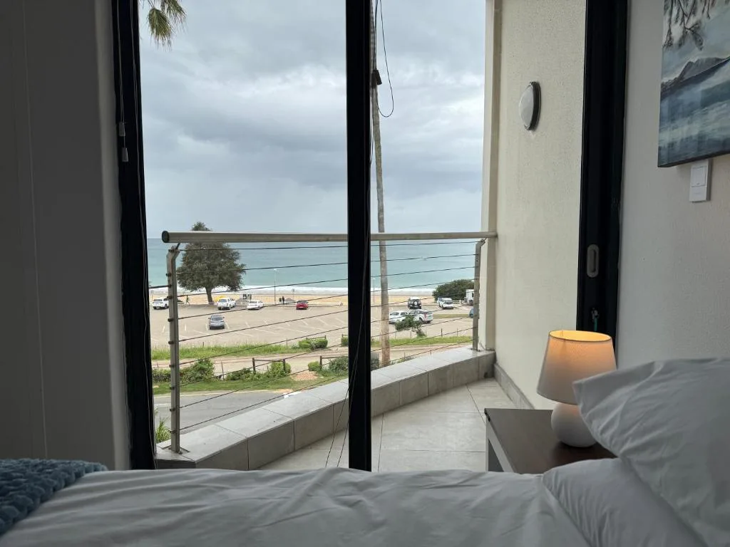 Bedroom with large windows overlooking beach and parking area
