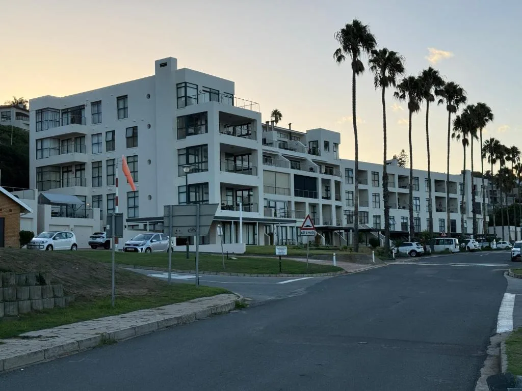 Modern white apartment building with palm trees and ocean-view balconies
