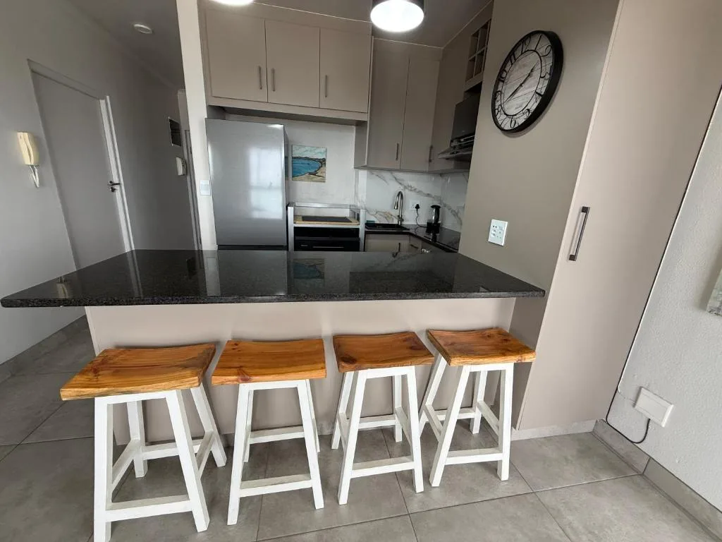 Modern kitchen with dark granite countertop, white cabinetry, and wooden bar stools
