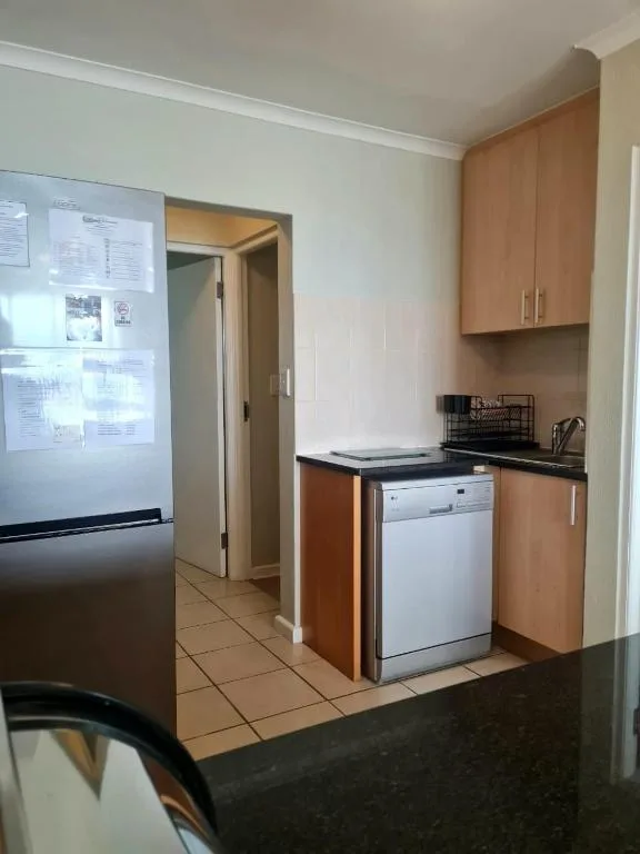 Compact kitchen with wooden cabinetry, stainless steel dishwasher, and refrigerator