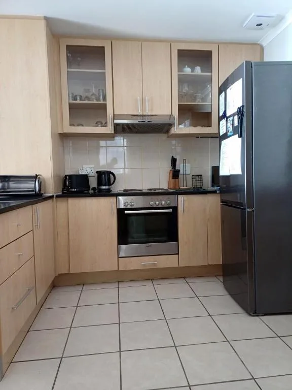 Modern kitchen with light wood cabinetry, stainless steel stove, and black refrigerator